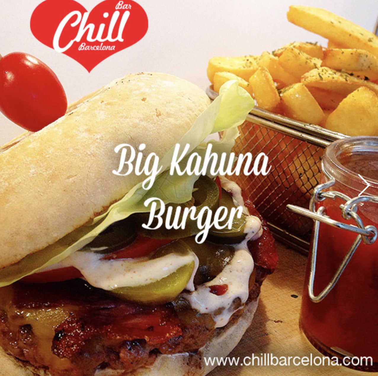 A large burger overflows with pickles and sauce beside a basket of fries. 