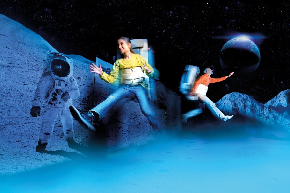 Smiling girl and older man are floating above the ground with space gear on in a moon landscape