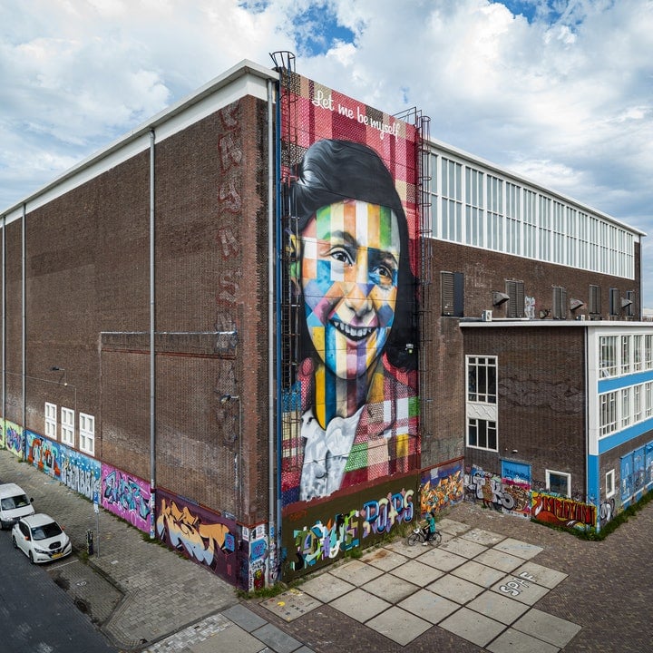 Colourful street art painting of Anne Frank on the side of a warehouse