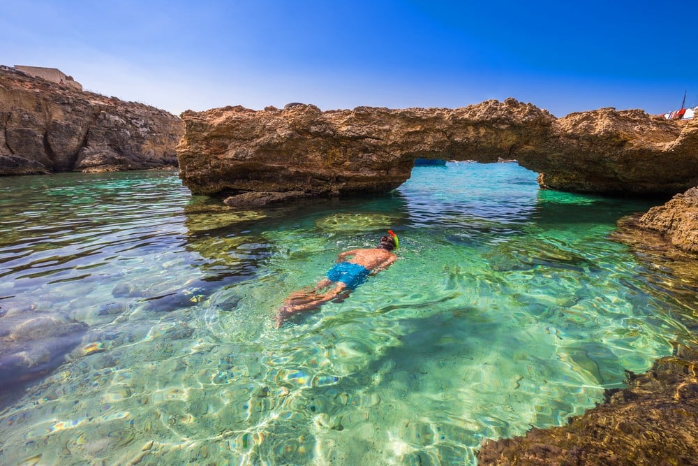 An image of a man snorkeling around crystal-clear water in Comino.