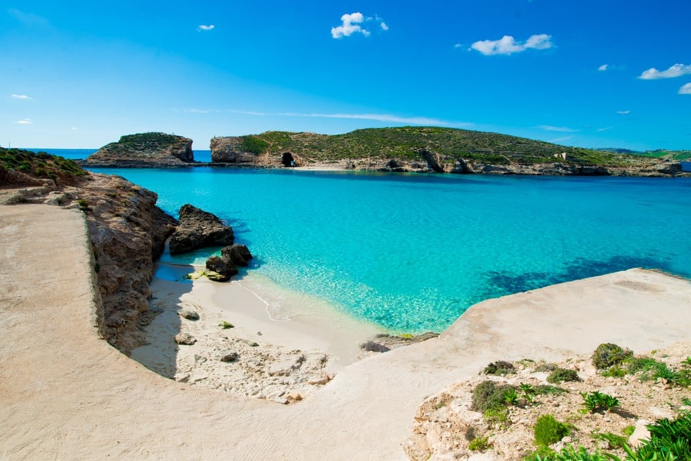 A view of Malta's Blue Lagoon with vibrant blue water and the iconic dome-shaped cave in the background.