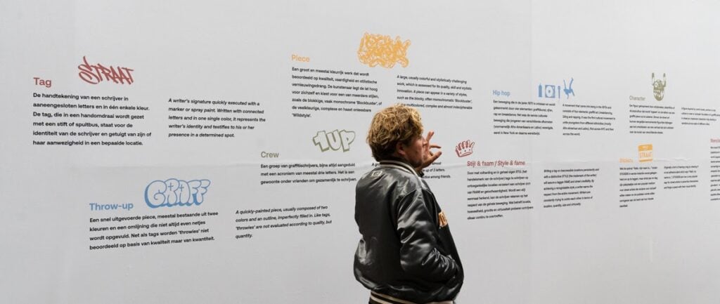 David Roos pointing at a wall at STRAAT Museum in Amsterdam, describing various words used in street art terminology.