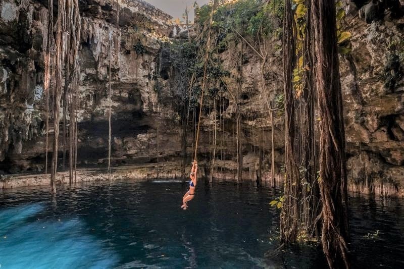 A woman hanging from a vine above a cenote pool, one of the best things to do in Tulum