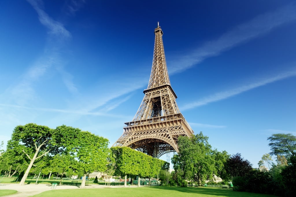 Eiffel Tower on a clear day with blue sky and sun shining on rows of trees