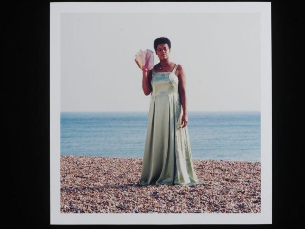A photograph of a woman holding a conch shell on the beach.