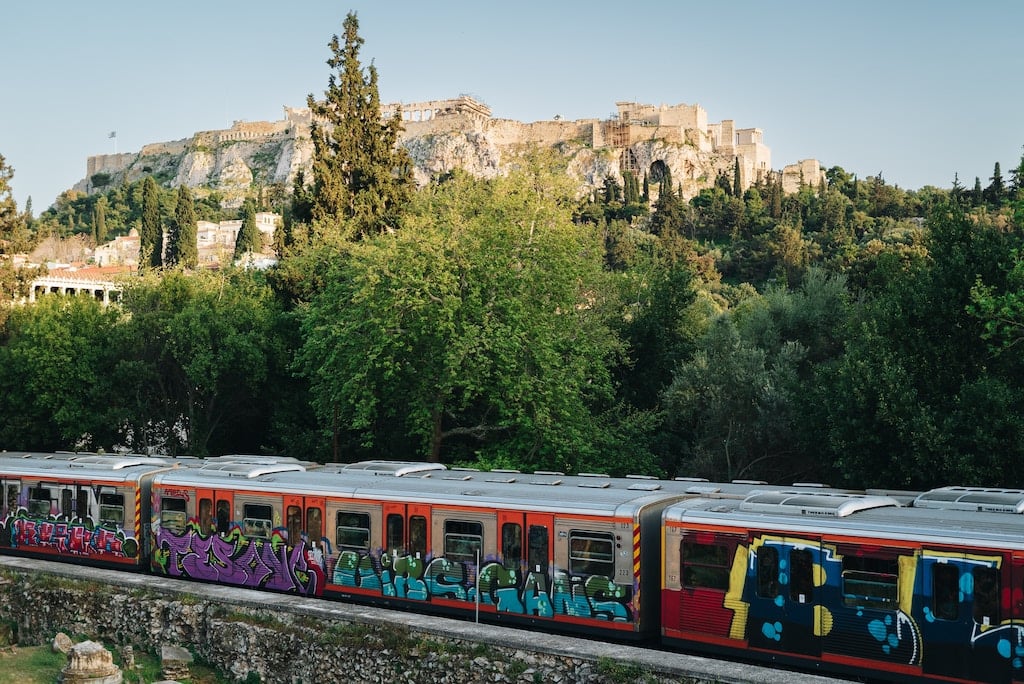 Several metro cars drive by at the base of the Athens Acropolis.