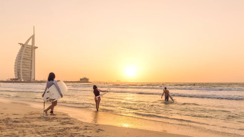 Surfers on the Dubai beach during dusk.