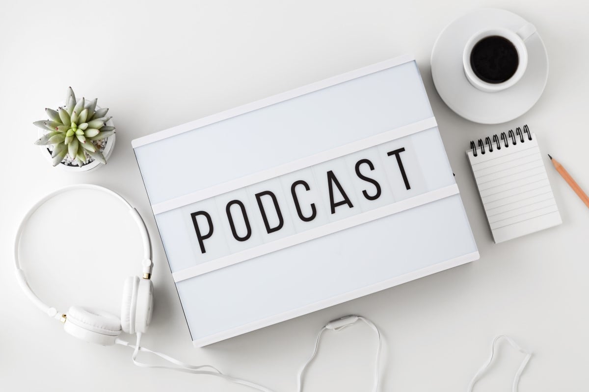 Podcast word on lightbox with headphones on white table, flat lay